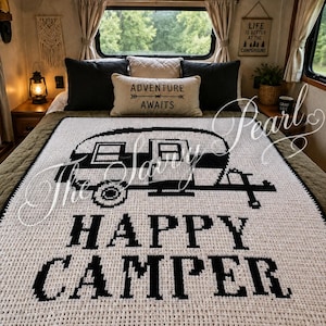 May include: A white and black crocheted blanket featuring a graphic of a vintage camper trailer and the text "HAPPY CAMPER" in a bold, block-style font. The blanket has a textured, grid-like stitch pattern and a solid black border edge.