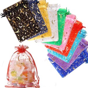 May include: A collection of sheer drawstring gift bags in various colors, including black, gold, and pink. Each bag is adorned with a gold celestial pattern of moons and stars. One bag is filled with colorful, square-shaped objects.