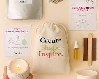 May include: A flat lay of a DIY terrazzo resin candle kit. The kit includes resin, a bag with the text "Create Shape Inspire", a candle, and other supplies. The candle is lit, and the kit is on a cream-colored surface.