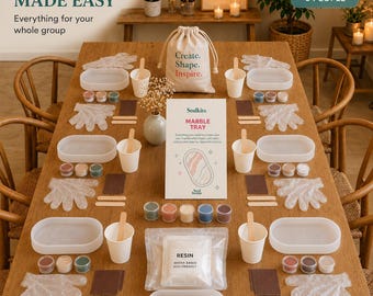 May include: A craft kit for six people featuring white oval trays, small cups of colored resin, mixing sticks, gloves, sandpaper, and a bag of resin powder. A central instruction card reads Stulkits Marble Tray, and a drawstring bag says Create. Shape. Inspire.