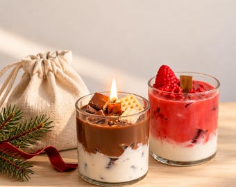 May include: Two glass candles in clear jars. One candle features a brown chocolate-colored top layer with chocolate pieces and a waffle, and a white bottom layer. The other candle has a red raspberry-colored top and a white bottom layer.