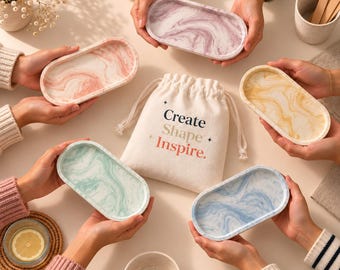 May include: Five oval trays with marbled patterns in pink, purple, yellow, green, and blue, arranged around a central cream-colored drawstring fabric pouch printed with the text Create Shape Inspire in black and orange lettering.