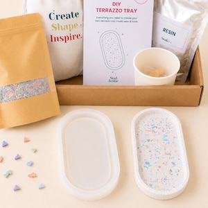 May include: A DIY terrazzo tray kit in a cardboard box containing a bag of colourful chips, a white instruction card with the text DIY TERRAZZO TRAY, a bag labelled RESIN, a paper cup, a translucent silicone oval mould, and a finished oval tray.