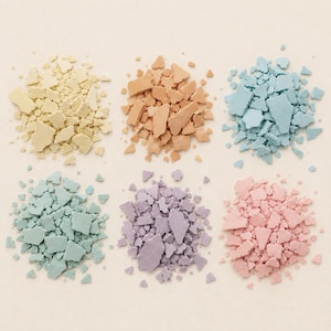 Puede incluir: Seis montones distintos de fragmentos de arcilla o tiza triturados con acabado mate, dispuestos en una cuadrícula. Los colores incluyen amarillo pálido, melocotón suave, azul claro, verde menta, lavanda y rosa pastel, con piezas irregulares.