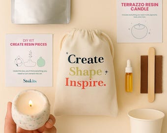 May include: A DIY resin craft kit with a candle, bag, and instructions. The bag reads "Create Shape Inspire." Other items include a bottle, mixing sticks, and a cup. The candle is lit and held in a speckled container.
