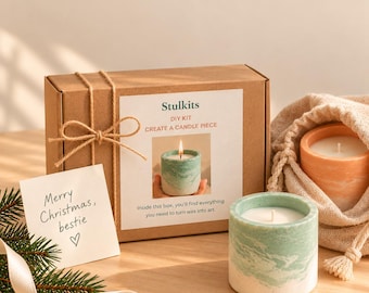 May include: A brown cardboard box tied with twine, labeled Stulkits DIY Kit Create a Candle Piece, next to a green marbled candle in a cylindrical container, a peach marbled candle in a fabric pouch, and a note reading Merry Christmas, bestie.