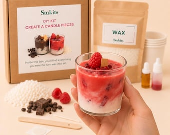 May include: A DIY candle making kit featuring a cardboard box labeled Stükits Create a Candle Pieces, a pouch of white wax beads, a glass container with a red and white layered candle, fresh raspberries, chocolate pieces, and a wooden stirrer.