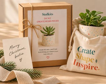 May include: A brown cardboard box labeled Stulkits DIY Kit Create Resin Pieces with twine, a cream-colored drawstring bag with the text Create Shape Inspire, a small succulent in a speckled pot, and a card reading Merry Christmas, bestie.