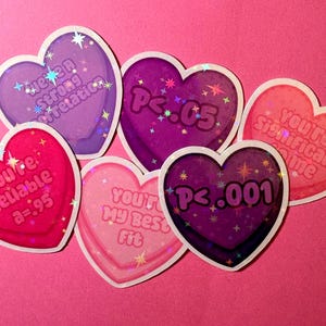 May include: A collection of heart-shaped stickers in shades of pink, purple, and red. Each sticker has a white border and features text such as "You're Reliable a=.95" and "P<.05". The background is a solid pink.