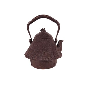 May include: A brown cast iron teapot with a thatched roof design. The teapot has a curved handle and a spout. The lid has a small knob. The teapot is a traditional Japanese style, and is likely used for tea ceremonies.