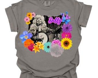 May include: Gray t-shirt featuring a black and white image of a woman playing a banjo, surrounded by colorful flowers and butterflies. The word "Dolly" is in pink script, and the text "Summie Digital Shop" is also visible.