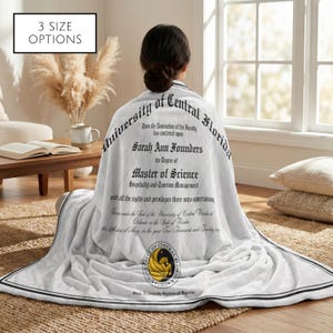 May include: A white blanket with black trim and text from the University of Central Florida. The blanket features the text "Sarah Ann Founders, Master of Science, Hospitality and Tourism Management." The image also includes the text "3 SIZE OPTIONS."