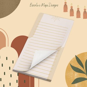 May include: A notepad with lined pages, a sun illustration, and a corner of the top page turned up. The notepad is set against a beige background with abstract shapes in brown and tan, and a decorative tassel garland.