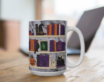 May include: White ceramic mug featuring a bookshelf design with Halloween-themed illustrations. The design includes books, a witch's hat, a raven, a jack-o'-lantern, a ghost, and a black cat. The mug is on a wooden surface.