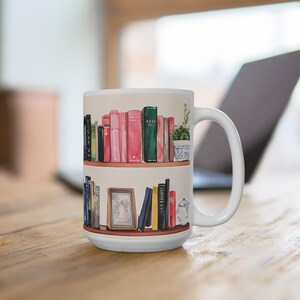 Könnte beinhalten: Weiße Keramik-Tasse mit einer Aquarell-Illustration von zwei Bücherregalen voller Bücher. Das obere Regal zeigt rosa und grüne Bücher, eine kleine Topfpflanze und den Text "KEAO MTC". Das untere Regal hat weitere Bücher und ein gerahmtes Bild.