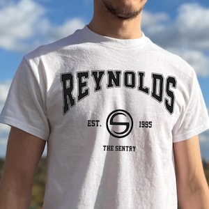 May include: White t-shirt with the word "REYNOLDS" arched across the chest in black block letters. Below the word "REYNOLDS" is the text "EST. 1995" and a circular logo with the letter "S" inside. The text "THE SENTRY" is below the logo.