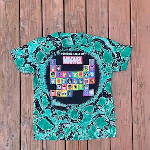 May include: A green and black tie-dye t-shirt featuring a graphic of the Marvel Comics periodic table. The design includes various superhero portraits within a black square, with the words "Periodic Table of Marvel" above.