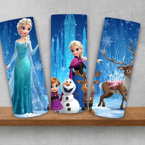 Puede incluir: Tres vasos cil&iacute;ndricos con personajes de Frozen. El primero muestra a Elsa con un vestido azul. El segundo muestra a Anna, Olaf y Sven. El tercero presenta un reno en un paisaje nevado con tonos azules, copos de nieve y un castillo de hielo.