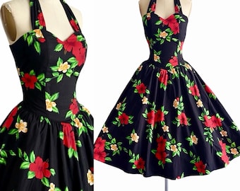 Pode incluir: Um vestido preto com decote halter apresentando uma estampa floral vibrante com grandes flores de hibisco vermelhas, flores amarelas menores e folhas verdes. O vestido tem um corpete justo com decote em coração e uma saia rodada.