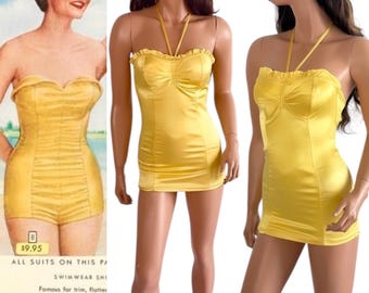 Pode incluir: Um fato de banho de cetim amarelo brilhante com decote em coração com acabamento em folhos, alça de pescoço e detalhes de costura vertical. A peça é exibida num manequim com um chapéu de sol de palha com uma fita preta.
