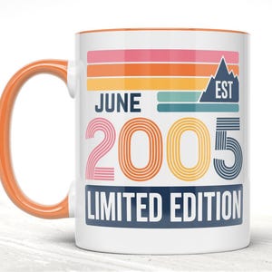 May include: White ceramic mug with an orange handle and rim. The mug features the text "JUNE 2005 LIMITED EDITION" in a retro design with a mountain graphic. The design includes pink, orange, blue, and green stripes.