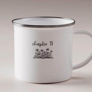 May include: White enamel mug with a silver rim and handle. The mug features the text "chapter 18" above a floral illustration of an open book. The design is in black. The mug is suitable for hot or cold drinks.