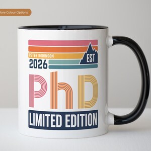 Könnte beinhalten: Weißer Keramikbecher mit schwarzem Henkel und Rand. Der Becher hat ein farbenfrohes Design mit dem Text "PhD LIMITED EDITION" und dem Jahr 2026. Das Design enthält eine Berg-Grafik und den Namen "Peter Robinson".