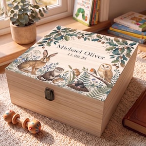 May include: A light-coloured wooden keepsake box with a metal latch, featuring a printed woodland scene with a rabbit, otter, mouse, mole, robin, and owl. The top is inscribed with the text Michael Oliver and the date 11.09.26 in black font.