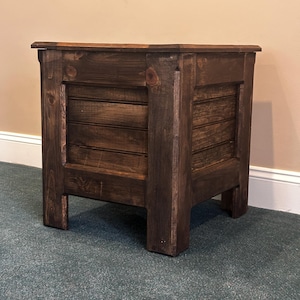 May include: A dark brown wooden side table with a rectangular shape. The table has a slatted design on the front and sides, with a solid top and four sturdy legs. The wood grain is visible, giving it a rustic appearance.