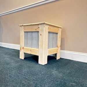 Puede incluir: Una pequeña mesa auxiliar cuadrada de madera. Construida con madera clara con un acabado natural. Los lados presentan paneles grises verticales. La mesa tiene cuatro patas robustas y un diseño sencillo y limpio. Dimensiones: aproximadamente 40 cm x 40 cm x 40 cm.