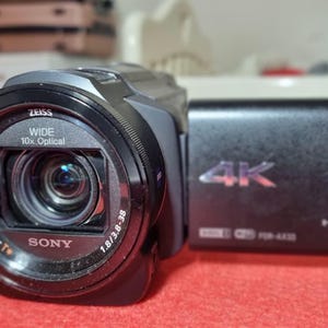 Op de afbeelding: Een zwarte Sony Handycam met een Zeiss-lens, met 10x optische zoom en 4K-resolutie. De camera heeft een zwarte behuizing met het Sony-logo en 20,6 megapixels. De lens heeft de tekst "Vario-Sonnar T*" erop.