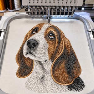Pode incluir: Um bastidor de máquina de bordar contendo um painel de tecido com um retrato detalhado de um cão tipo sabujo costurado à máquina. O cão apresenta pelagem castanha, preta e branca, orelhas longas e caídas e grandes olhos castanhos.