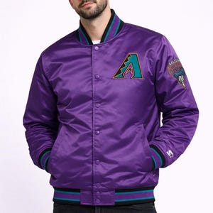 May include: Purple satin baseball jacket with the Arizona Diamondbacks logo on the chest. The jacket has a button-up front, black and teal striped trim, and a team logo patch on the sleeve. A classic sports apparel item.