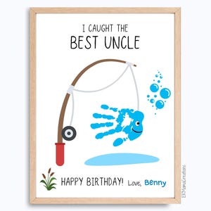 Puede incluir: Una impresión enmarcada con el texto "I Caught the Best Uncle". Un pez azul con forma de huella de mano está en una línea de pesca. Las palabras "Happy Birthday! Love, Benny" están en la parte inferior. La obra de arte está en un marco de madera.