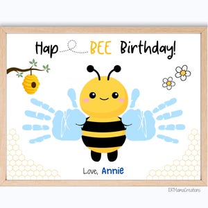 May include: A framed print with a cartoon bee design. The bee is yellow and black, with blue handprint wings. Text reads "Hap BEE Birthday!" and "Love, Annie". Includes a small beehive and flowers.