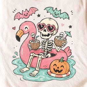 May include: A cream-colored t-shirt featuring a graphic of a skeleton wearing heart-shaped sunglasses, sitting in a pink flamingo pool float in turquoise water. The skeleton holds two coconut drinks, while a jack-o'-lantern and two bats appear.