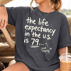 May include: A white ceramic mug with a black handle and the text "But First, Coffee" in a black, handwritten-style font. The mug is on a white surface.