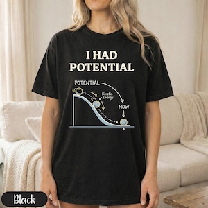 May include: Black t-shirt with the text "I HAD POTENTIAL" above a diagram illustrating potential and kinetic energy. The diagram shows a ball rolling down a curved path. The shirt is a dark color.