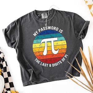 May include: Dark grey t-shirt with a colourful graphic. The graphic features a white Pi symbol inside a rainbow circle, surrounded by mathematical symbols and the text "MY PASSWORD IS THE LAST 8 DIGITS OF PI."