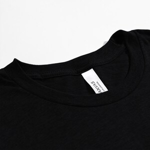 May include: Close-up of a black crew neck t-shirt. The shirt has a white tag on the inside collar with the text "ANVAS L.A. CANVAS."