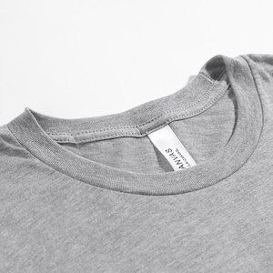 Op de afbeelding: Close-up van een grijze t-shirt halslijn. Het shirt heeft een ronde hals en een label met de tekst "ANVAS LA CANVAS". De stof lijkt zacht en de stiksels zijn zichtbaar.