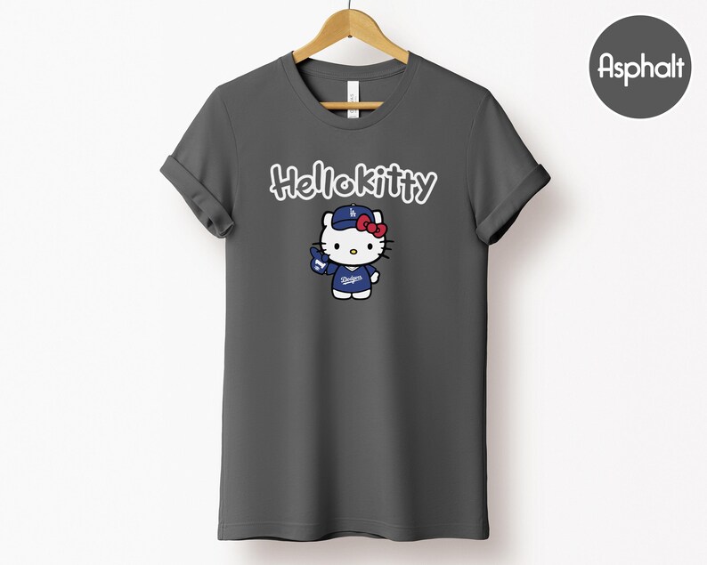 May include: Dark grey t-shirt with a Hello Kitty graphic. The graphic depicts Hello Kitty in a baseball cap and uniform with the text "Dodgers". The words "Hello Kitty" are written above the graphic in white script.