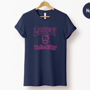 Op de afbeelding: Marineblauw T-shirt met opgerolde mouwen. Het shirt heeft de tekst "LOUEY" boven een Hello Kitty-afbeelding, met "Hellokitty" eronder in roze. Het T-shirt hangt aan een houten hanger tegen een witte achtergrond.