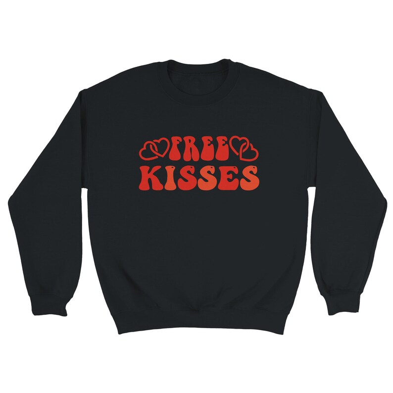 May include: Black sweatshirt featuring the text "FREE KISSES" in a retro style. The lettering is in shades of red and orange, with heart motifs. A relaxed, comfortable garment.