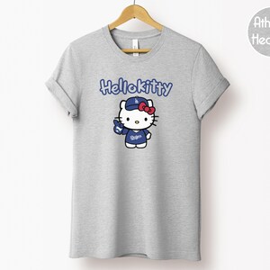 May include: Grey athletic t-shirt with a Hello Kitty graphic wearing a baseball uniform. The text "HelloKitty" is above the graphic. The graphic includes a blue baseball cap and uniform with the word "Dodgers".