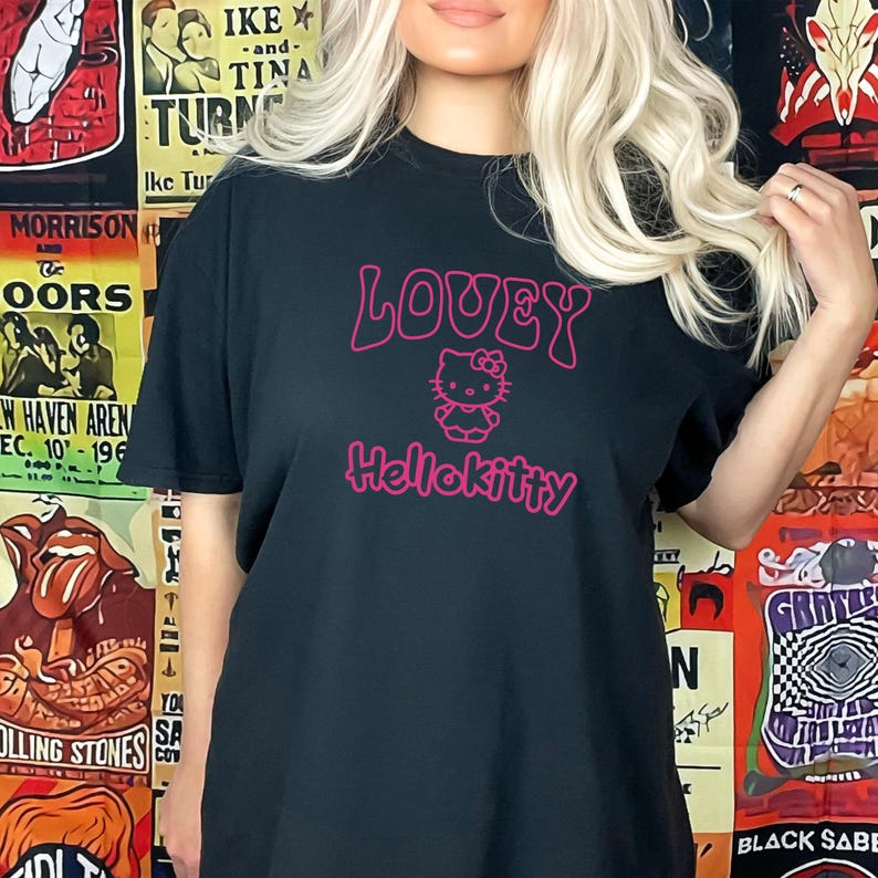 Op de afbeelding: Zwart T-shirt met het woord "LOVEY" boven een Hello Kitty-afbeelding en het woord "Hellokitty" in roze. Het shirt is een casual stijl, geschikt voor dagelijks gebruik.