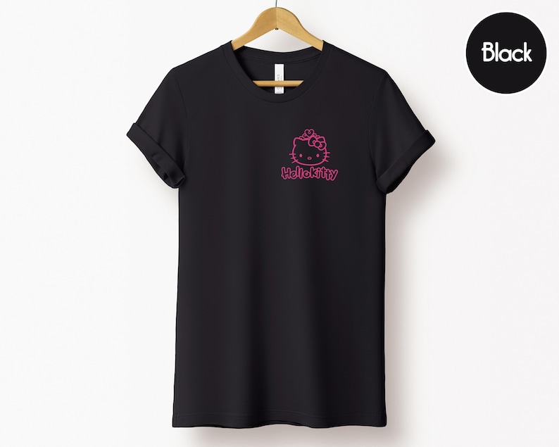 May include: Black t-shirt with a pink Hello Kitty graphic on the front. The t-shirt is hanging on a wooden hanger against a white background. The word "Black" is in a black circle in the upper right corner.