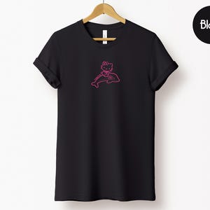 May include: Black t-shirt with a pink graphic of a cartoon cat riding a dolphin. The cat is wearing a bow and the dolphin is outlined in pink. The word "Black" is in a black circle in the upper right corner.