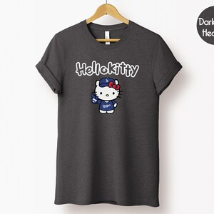 May include: Dark grey heather t-shirt with a Hello Kitty graphic. The graphic shows Hello Kitty wearing a baseball cap and jersey with the text "Dodgers". The text "Hello Kitty" is above the graphic in white.