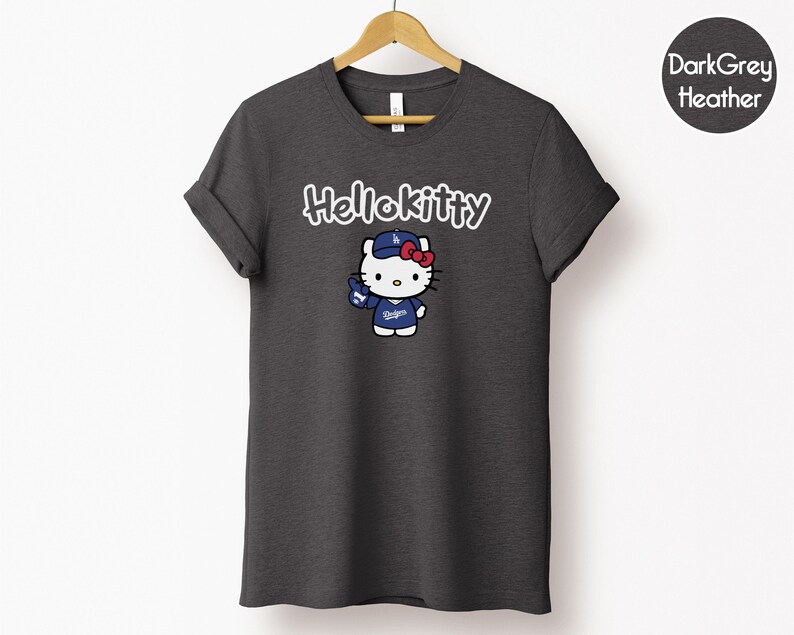 May include: Dark grey heather t-shirt with a Hello Kitty graphic. The graphic shows Hello Kitty wearing a baseball cap and jersey with the text "Dodgers". The text "Hello Kitty" is above the graphic in white.